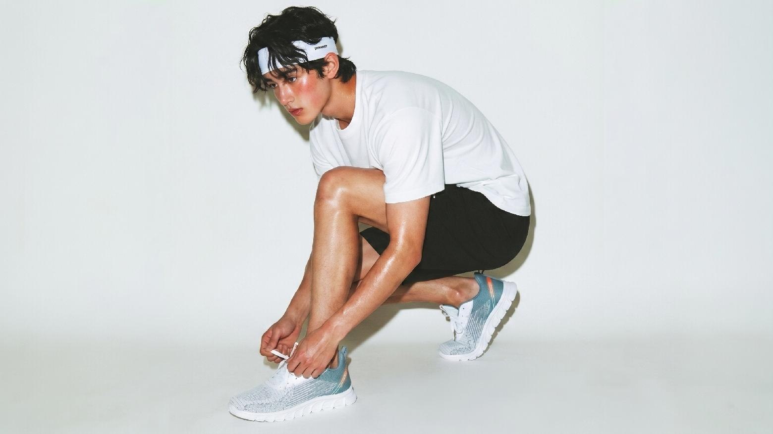 A runner in a white shirt tying a gray running shoe in a light studio